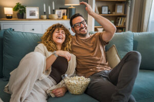 a couple laughs and shares popcorn on the couch