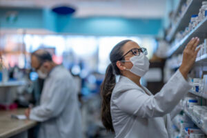 Woman working at a pharmacy getting something from a shelf wearing a mask