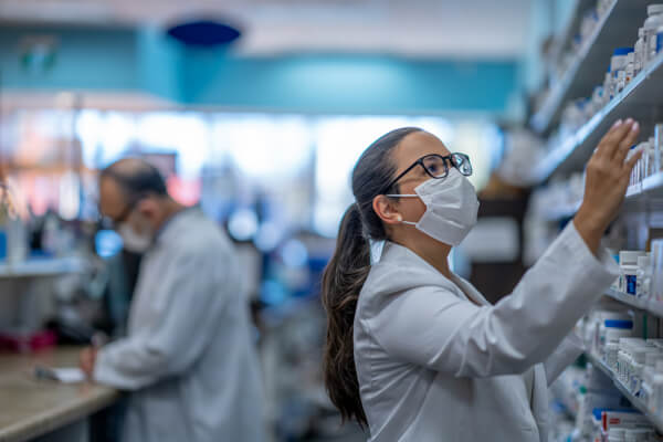 Woman working at a pharmacy getting something from a shelf wearing a mask