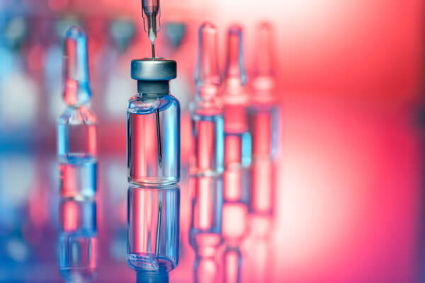 Needle extracting medication from bottle against a bright background