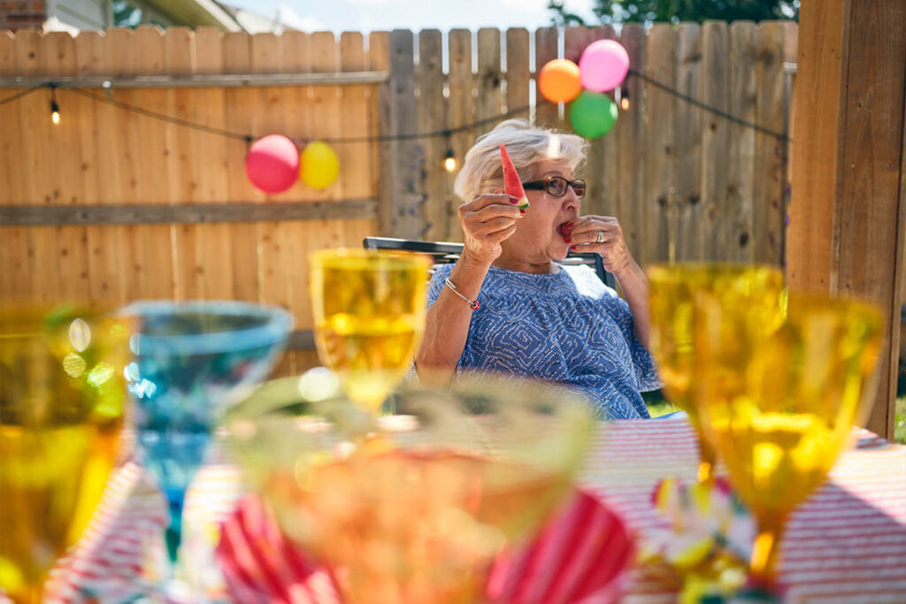 an older woman at an outdoor party eats a strawberry